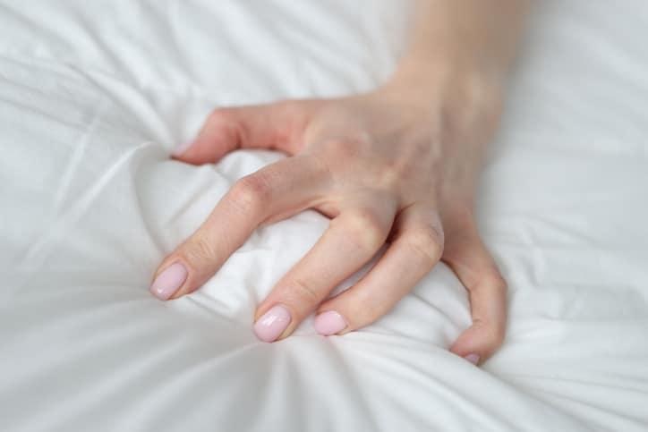 Woman hand squeezing white blanket at home closeup. Female orgasm concept