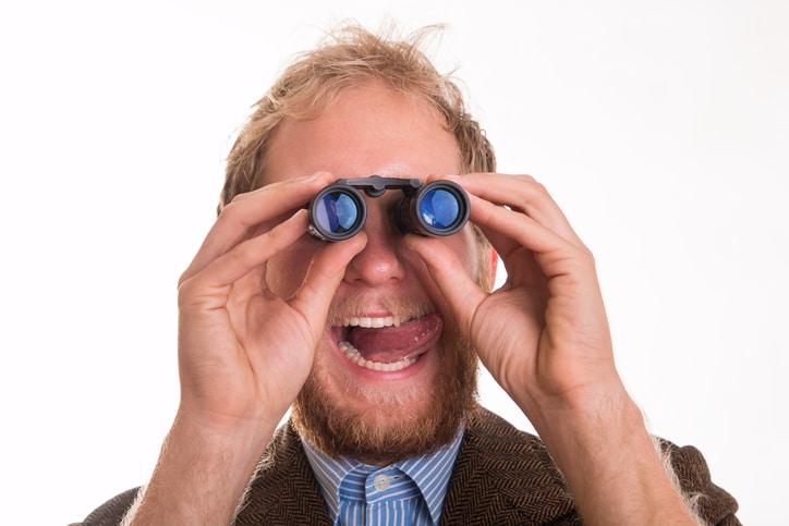 Pervert voyeur man watching someone through binoculars - studio shot