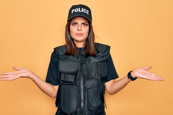 Young beautiful brunette policewoman wearing police uniform bulletproof and cap clueless and confused with open arms, no idea concept.